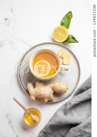 A cup of hot tea with fresh lemon and ginger on a plate on a light marble background A cup of hot tea with fresh lemon and ginger on a plate on a light marble background 134831596