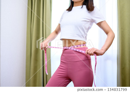 Japanese woman measuring her waist with a tape measure while wearing yoga wear, diet leggings Japanese woman measuring her waist with a tape measure while wearing yoga wear, diet leggings 134831799