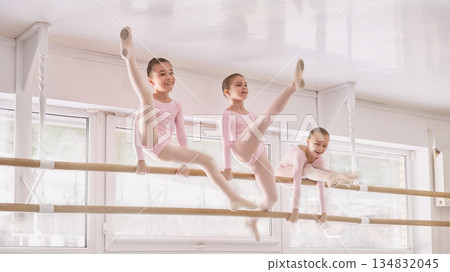 Young ballet students performing inverted stretching at barre in studio 134832045