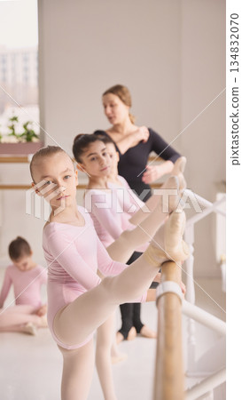 Young ballerina stretching leg at barre during ballet training session. 134832070