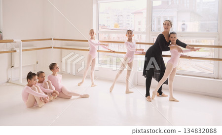 Ballet teacher assisting students during balance exercise at dance studio. 134832088