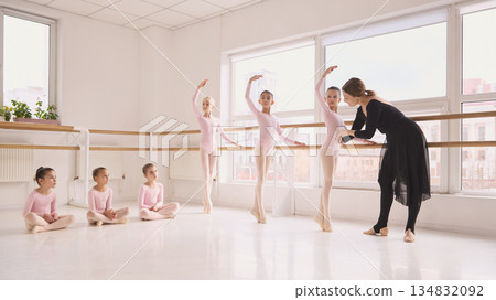 Ballet instructor correcting posture of child dancer during barre exercise. 134832092