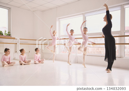 Young ballet students practicing basic positions at barre in dance studio. Young ballet students practicing basic positions at barre in dance studio. 134832093