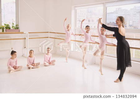 Ballet teacher guiding young girls during classical dance class at barre. 134832094