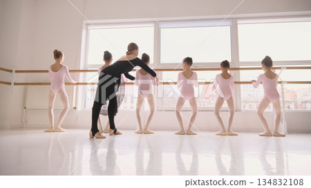 Ballet teacher demonstrating arm movement to children at barre. 134832108