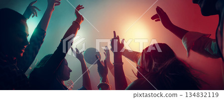 Energetic nightclub crowd with raised hands under neon lights. 134832119