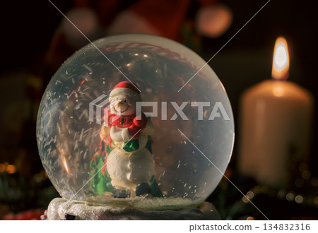 Snow Globe with Snowman and Christmas Tree in Warm Candlelit Holiday Setting Snow Globe with Snowman and Christmas Tree in Warm Candlelit Holiday Setting 134832316