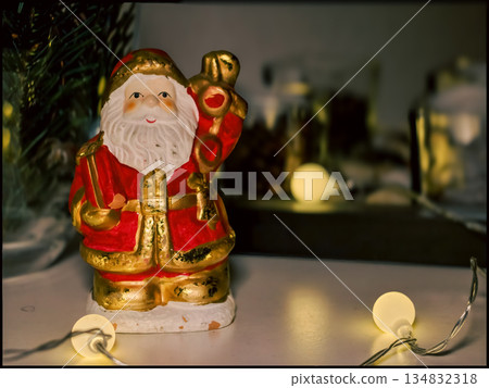 Santa Claus Figurine in Cozy Christmas Setting with String Lights and Decor Santa Claus Figurine in Cozy Christmas Setting with String Lights and Decor 134832318