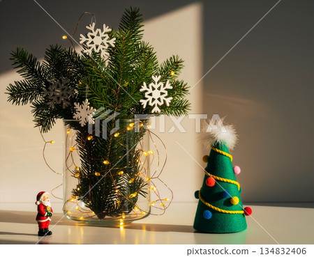 Glass Vase with Pine and Snowflakes, Felt Tree and Santa Figurine on White Surface with Shadows 134832406