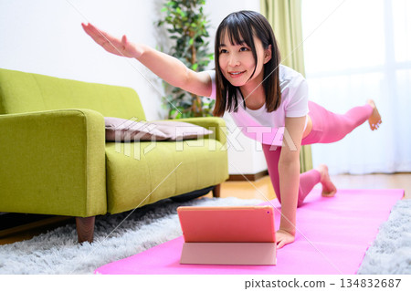 獵犬：一位年輕女子在家中一邊用平板電腦觀看 YouTube 視頻，一邊做瑜伽。身穿瑜珈服。 134832687