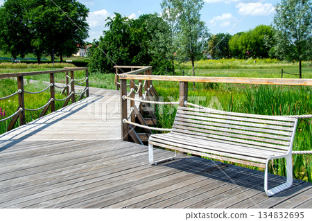 A wooden bench is on a boardwalk with a fence and trees in the background. High quality photo A wooden bench is on a boardwalk with a fence and trees in the background. High quality photo 134832695