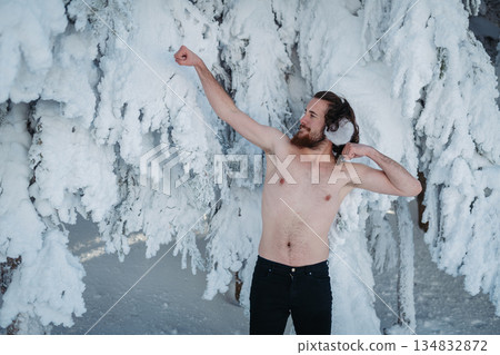 Man with bare torso standing in front of snow covered trees. 134832872