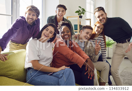 Happy young diverse friends sitting on sofa at home looking cheerful at camera enjoying meeting Happy young diverse friends sitting on sofa at home looking cheerful at camera enjoying meeting 134833912
