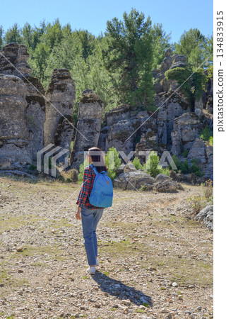 A woman tourist with a backpack on her back walks through the ancient city of Selga, admiring the wonderful nature and wonderful rocks. Turkey, Antalya. 134833915
