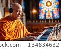 A Buddhist monk in orange robes serenely plays a keyboard while wearing headphones, creating a peaceful atmosphere within a church 134834632