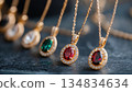 Elegant gold necklaces with vibrant gemstone pendants, showcasing red, green, and clear stones, displayed on a dark surface 134834634