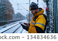 A railway worker checks a tablet computer during a snowy winter day on the railway tracks 134834636