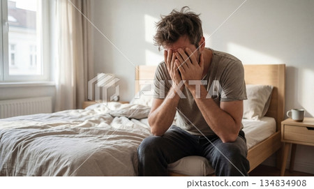 Stressed man sitting on bed holding his head, anxiety and burnout concept 134834908