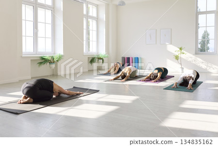 Group yoga class in Childs Pose within bright, serene studio filled with sunlight beams Group yoga class in Childs Pose within bright, serene studio filled with sunlight beams 134835162