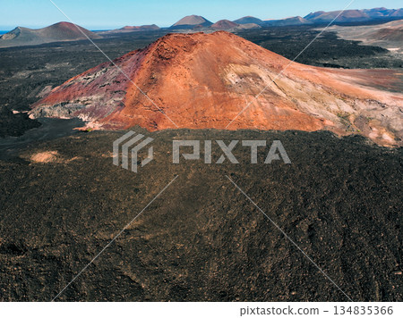A red mountain, black volcanic ground and lava formations, volcanoes on Lanzarote island. A red mountain, black volcanic ground and lava formations, volcanoes on Lanzarote island. 134835366