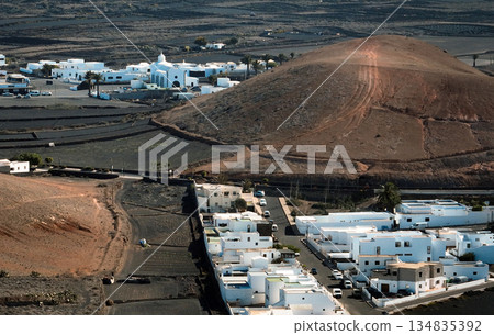 White buildings, town among volcanic black mountains and lava formations in Lanzarote, Canary Islands. 134835392
