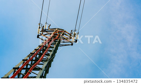 High voltage transmission tower. Energy flows through insulated cables in open sky. Power delivery for surrounding communities. Modern electrical distribution. Industrial transmission structure. 134835472