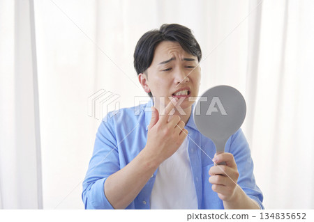 A man in his 20s suffering from tooth decay looking in the mirror A man in his 20s suffering from tooth decay looking in the mirror 134835652