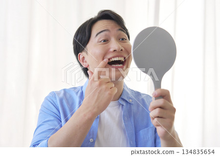 Man in his 20s looking in the mirror, dental care Man in his 20s looking in the mirror, dental care 134835654