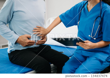 Senior Doctor discussing treatment with male patient talking and laughing sitting on examination bed 134837474