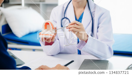 Dentist sitting at table with jaw samples tooth model and working with tablet and laptop in dental office professional dental clinic. 134837721