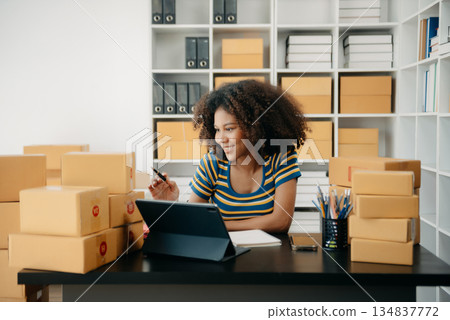 Startup small business SME, Entrepreneur owner African woman using smartphone or tablet taking receive and checking online purchase shopping order Startup small business SME, Entrepreneur owner African woman using smartphone or tablet taking receive and checking online purchase shopping order 134837772