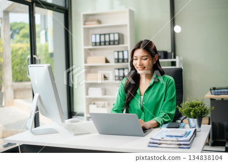 Asian woman using laptop and tablet while sitting at her working place. Concentrated Asian woman using laptop and tablet while sitting at her working place. Concentrated 134838104