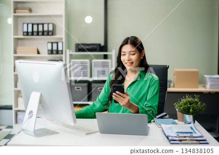 Asian woman using laptop and tablet while sitting at her working place. Concentrated Asian woman using laptop and tablet while sitting at her working place. Concentrated 134838105