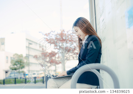 一名日本女大學生在公車站使用筆記型電腦 134839025