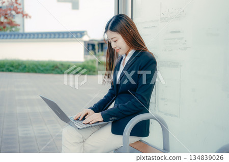 一名日本女大學生在公車站使用筆記型電腦 134839026
