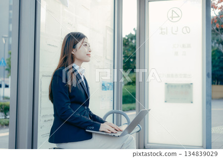 一名日本女大學生在公車站使用筆記型電腦 一名日本女大學生在公車站使用筆記型電腦 134839029