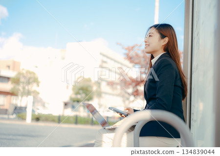 Japanese female university student using laptop and smartphone at bus stop Japanese female university student using laptop and smartphone at bus stop 134839044