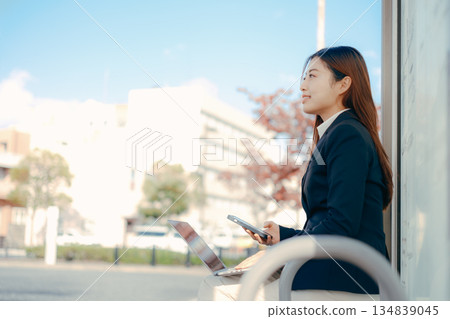 Japanese female university student using laptop and smartphone at bus stop 134839045