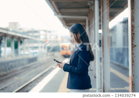 A Japanese female university student waiting for a train on the station platform with her smartphone in hand 134839274