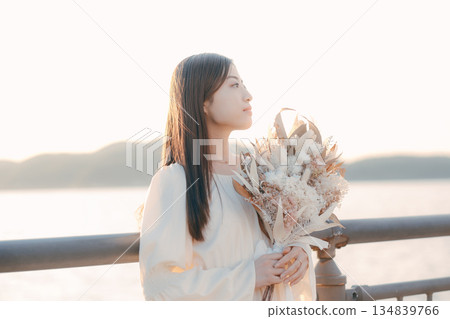 一位日本女子手捧乾花,站在海邊。 一位日本女子手捧乾花,站在海邊。 134839766
