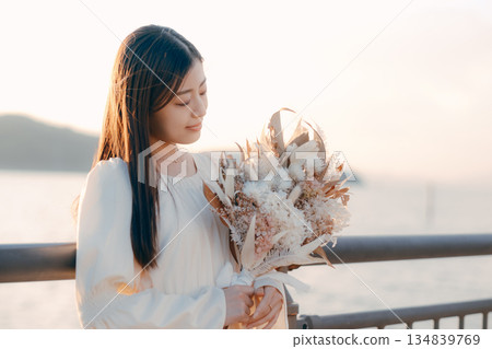 一位日本女子手捧乾花,站在海邊。 一位日本女子手捧乾花,站在海邊。 134839769