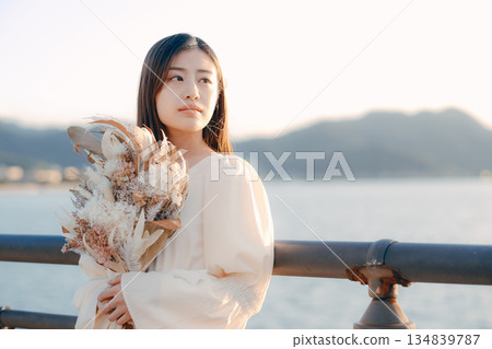 一位日本女子手捧乾花，站在海邊。 134839787