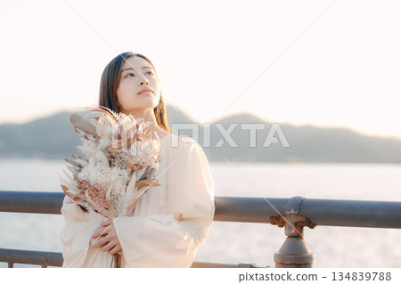 一位日本女子手捧乾花,站在海邊。 一位日本女子手捧乾花,站在海邊。 134839788