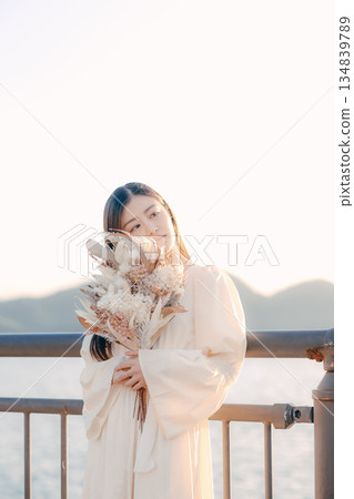 一位日本女子手捧乾花，站在海邊。 134839789