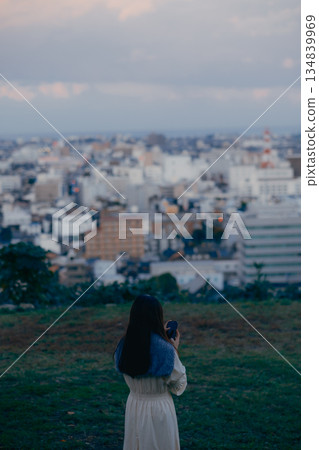 一位日本女性背對著鏡頭，用智慧型手機拍攝城市景觀。 134839969