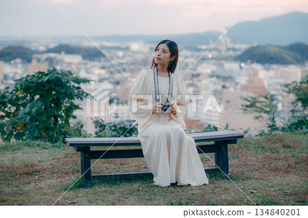 A Japanese woman standing with a film camera in hand with the cityscape in the background A Japanese woman standing with a film camera in hand with the cityscape in the background 134840201