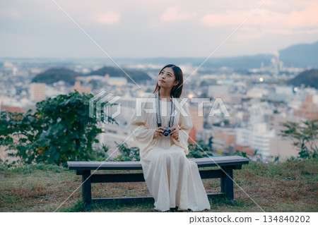 A Japanese woman standing with a film camera in hand with the cityscape in the background 134840202