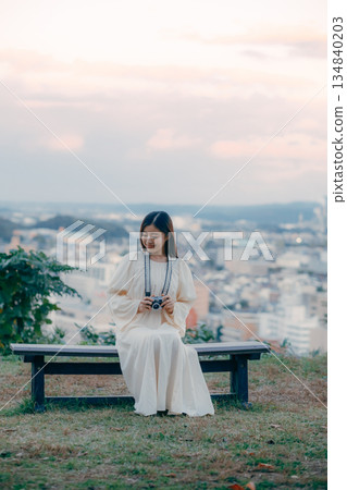 A Japanese woman standing with a film camera in hand with the cityscape in the background 134840203