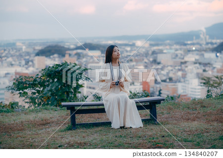 A Japanese woman standing with a film camera in hand with the cityscape in the background 134840207