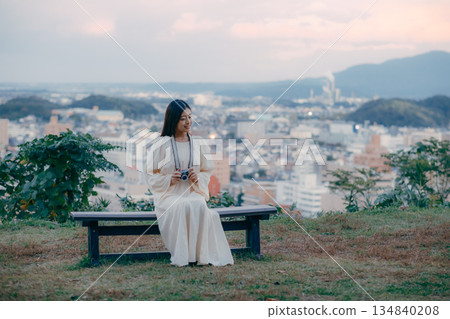 A Japanese woman standing with a film camera in hand with the cityscape in the background 134840208